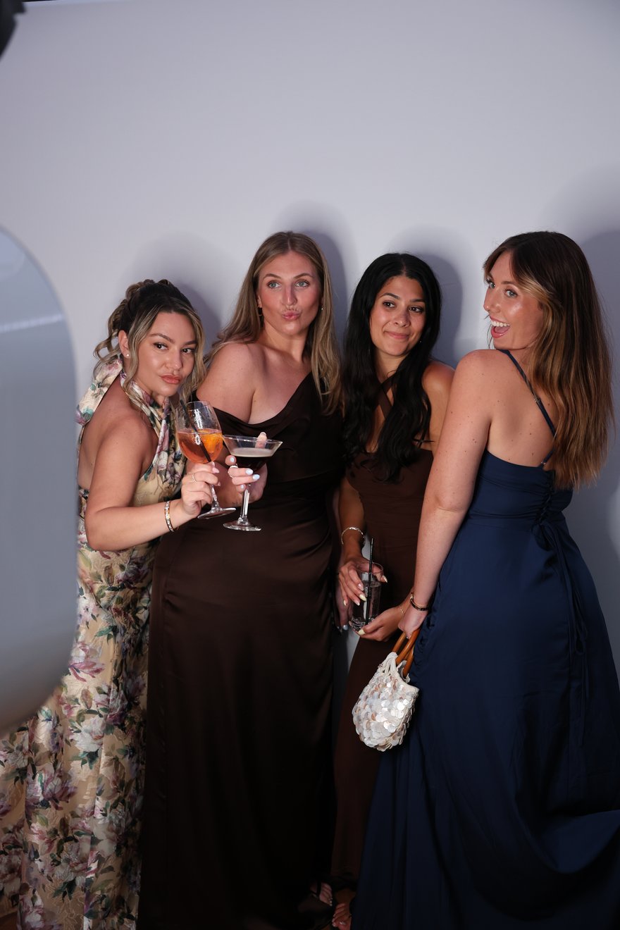 Four women with cocktails posing together on a soft grey backdrop