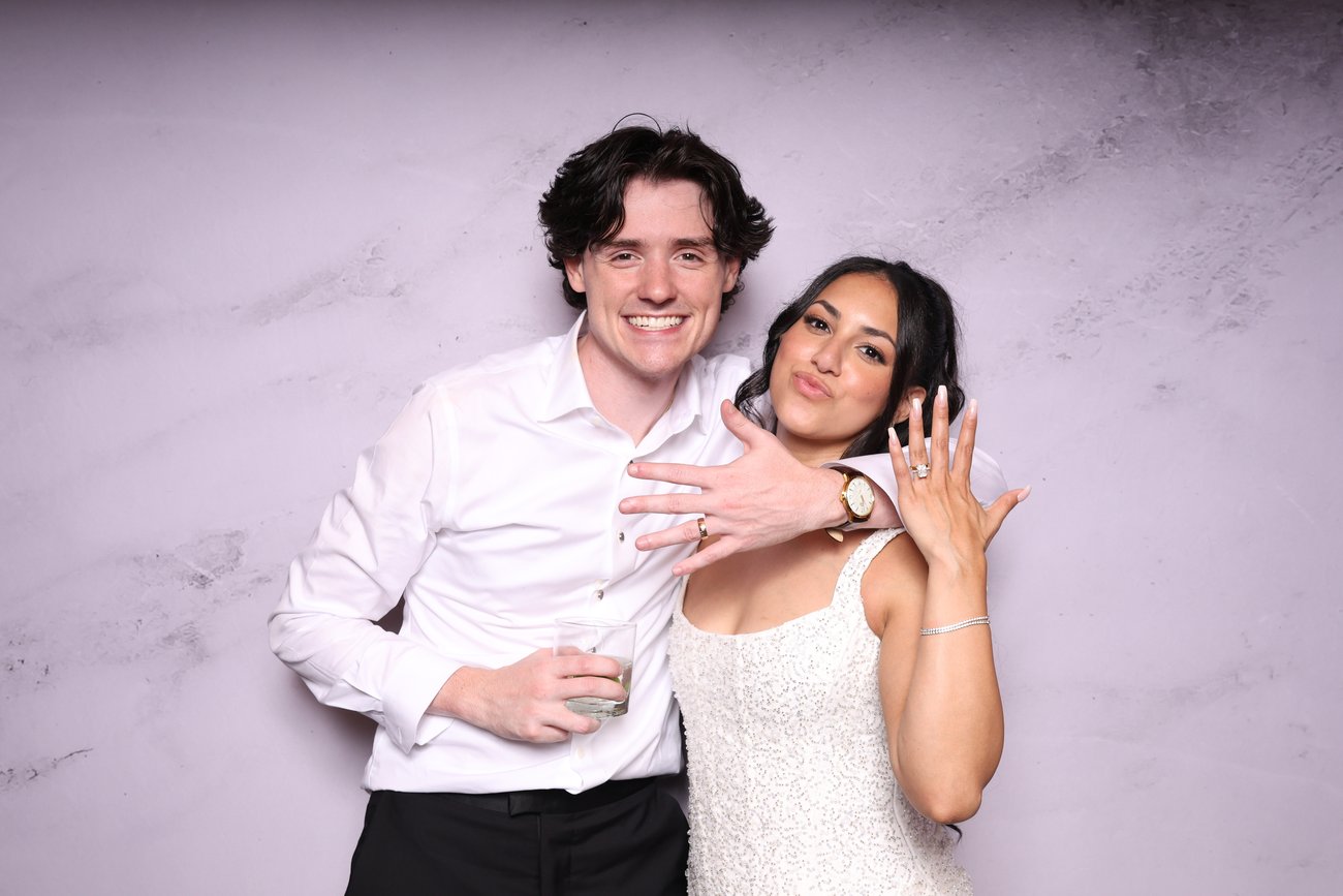 A couple showing off a ring in front of a marble backdrop