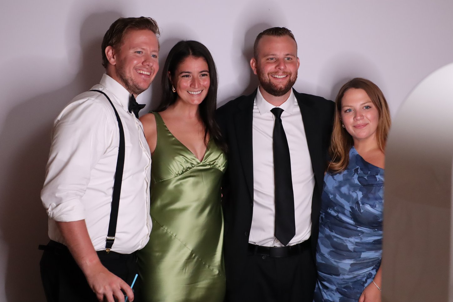 Four guests in cocktail attire posing together on a white backdrop