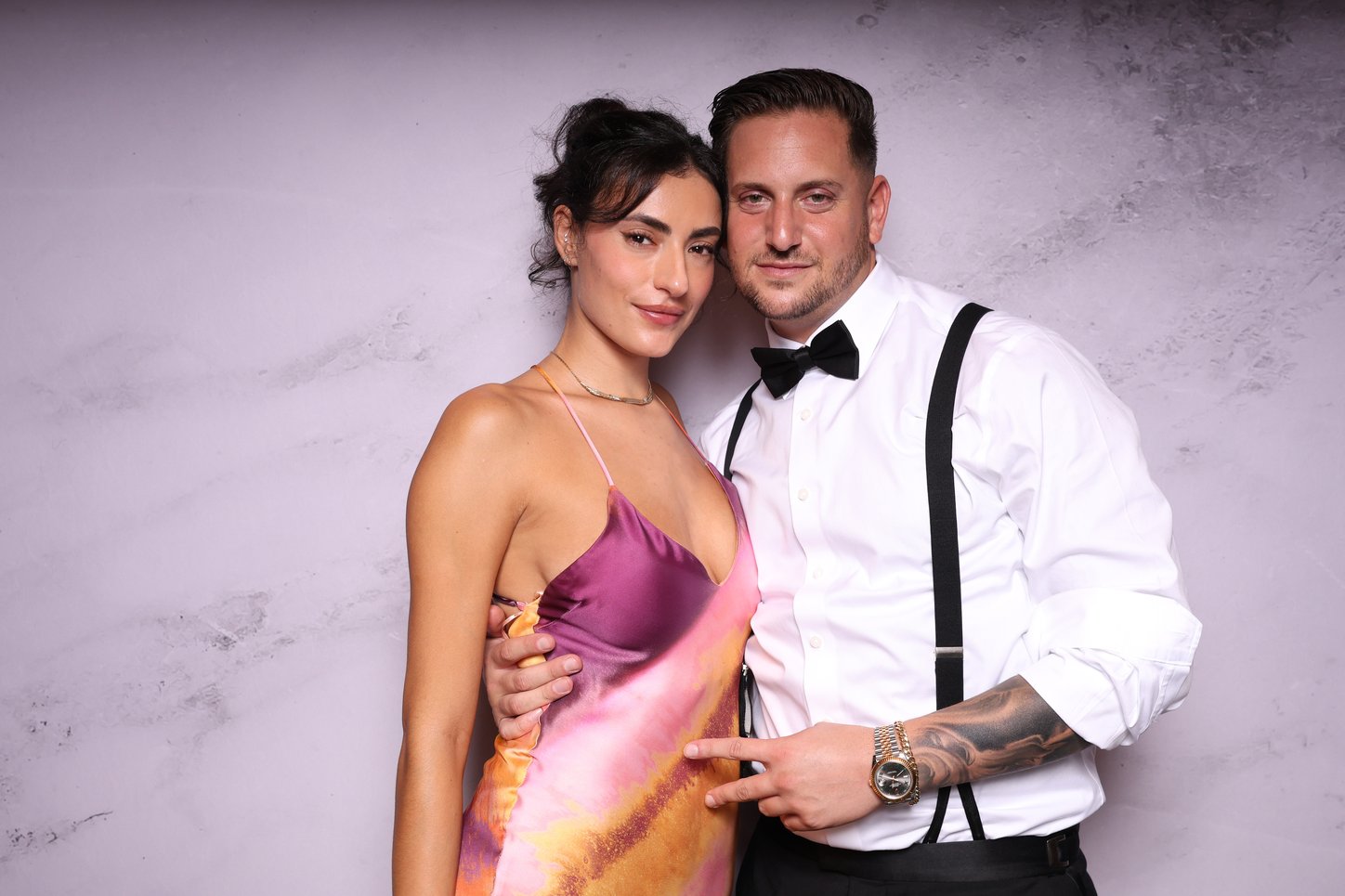 A couple in a bow tie and satin dress posing in front of a marble backdrop