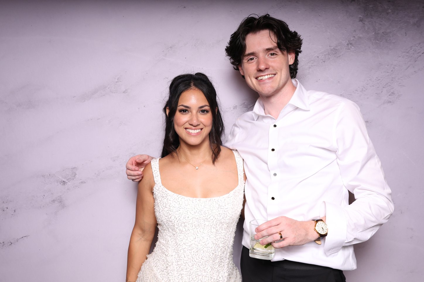A couple in a white shirt and white dress posing in front of a marble backdrop