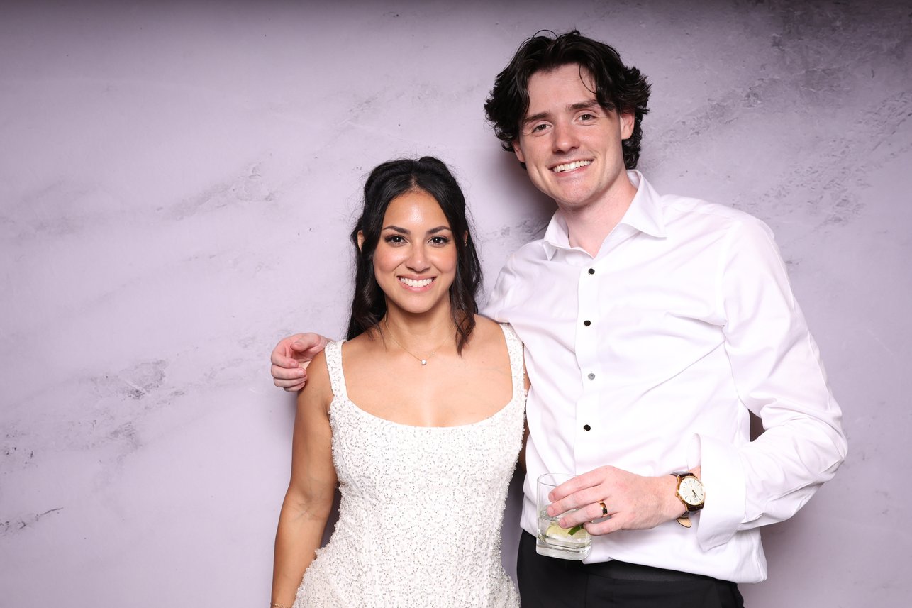 A couple in a white shirt and white dress posing in front of a marble backdrop