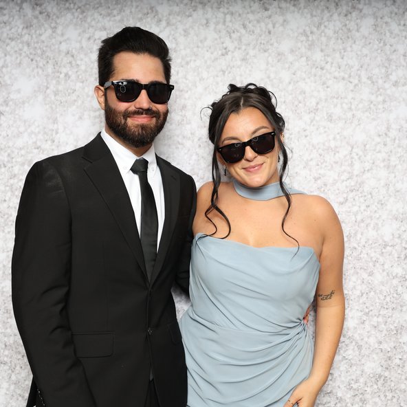 A couple in sunglasses posing in front of a sparkle backdrop