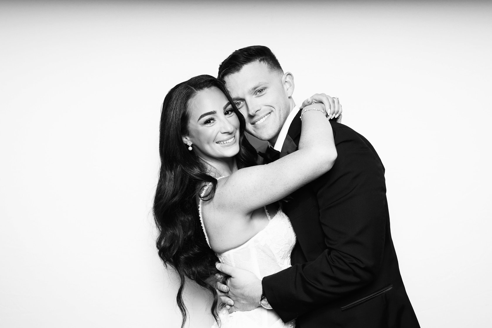 Black and white photo of a couple hugging in front of a white backdrop